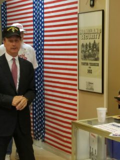 Fixler stands before an American flag and a poster celebrating native American warriors.